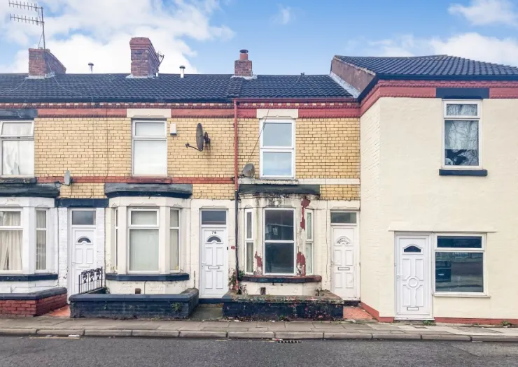 Attached terraced house with yellow brick, white trim, and bay window, needing renovation.