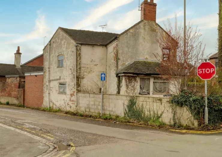 Exterior of weathered, detached house with crumbling render and overgrown vines.