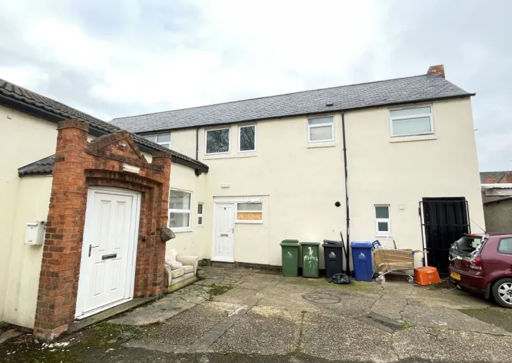 Cream two-story building exterior with brick entryway and discarded furniture and bins in the yard.