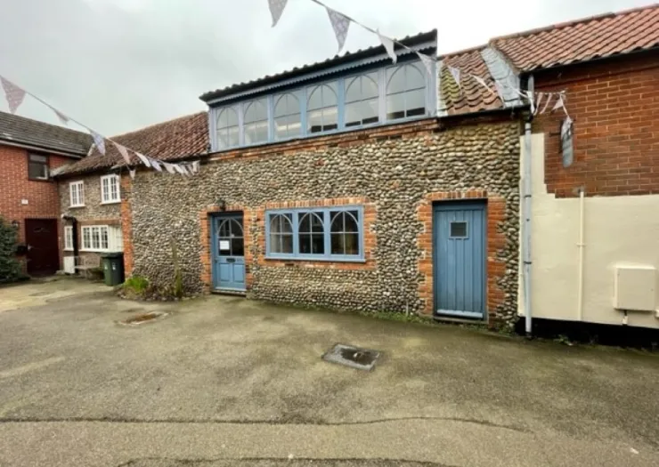 Charming pebble and brick building with blue doors and arched windows. Bunting strung overhead. Paved courtyard.