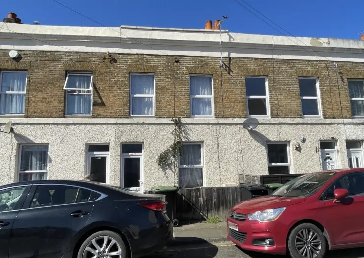 Terraced house exterior with yellow brick upper level and white ground floor, viewed from street on sunny day.