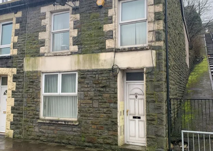 Stone terraced house exterior with white front door and steps leading uphill beside it.