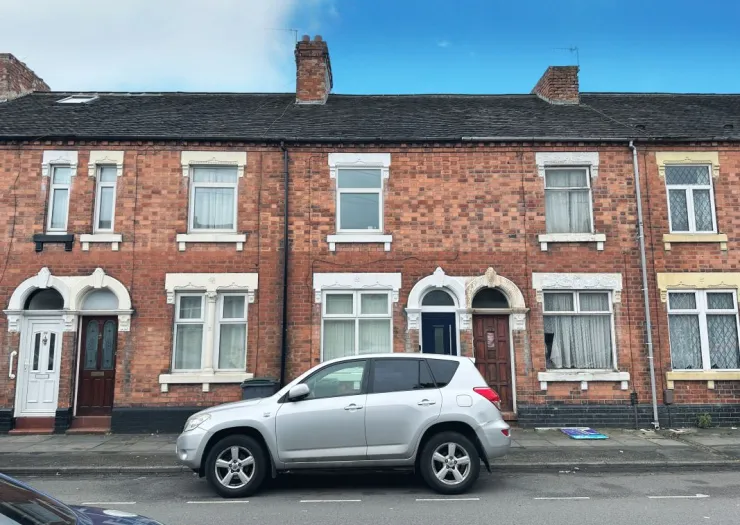 Red brick terraced house exterior with white window frames and a silver car parked on the street.