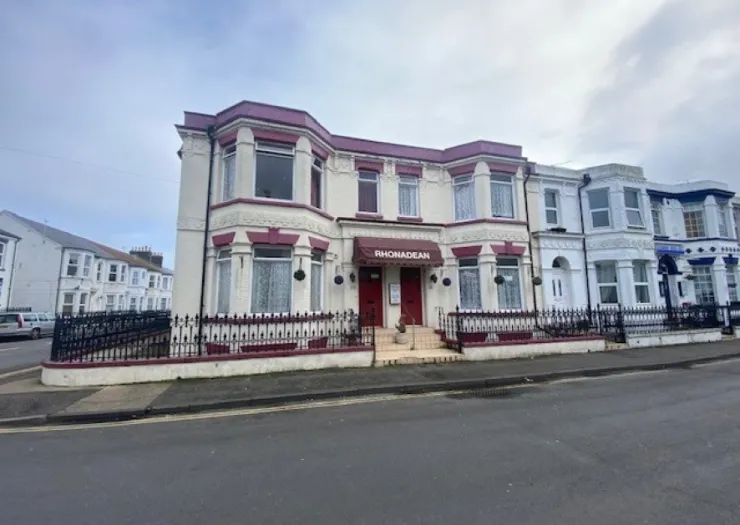 Rhonadean" guest house exterior with burgundy awning and decorative iron fence.