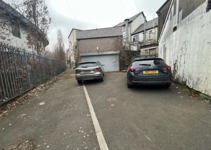 Back alley parking area with two cars and a garage door.