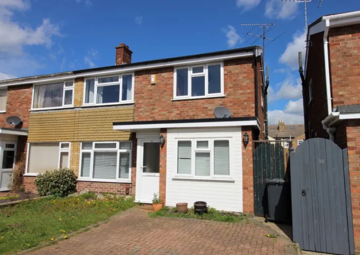 Two-story brick house with white extension, front garden, and paved driveway.