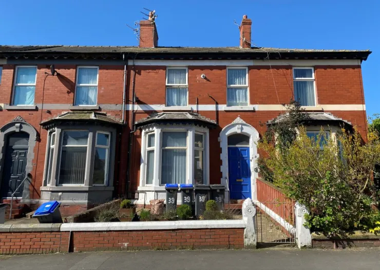 Red brick terraced house with bay window and blue front door.