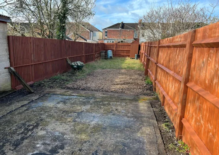 Long, narrow backyard with wooden fences, concrete pad, and small grassy area.