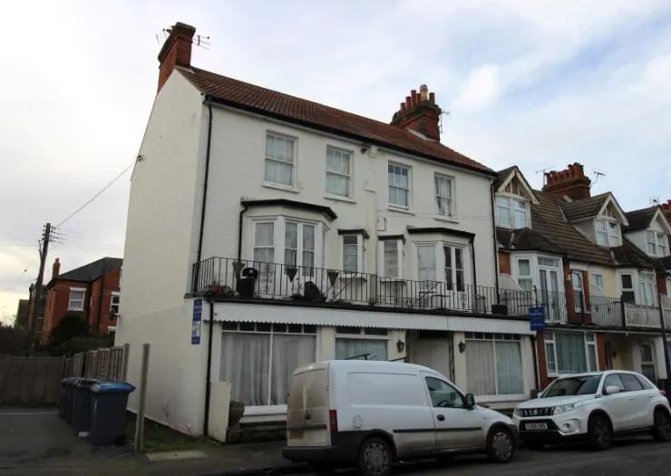 White two-story building with bay windows, a balcony, and a red tile roof. A white van is parked in front.