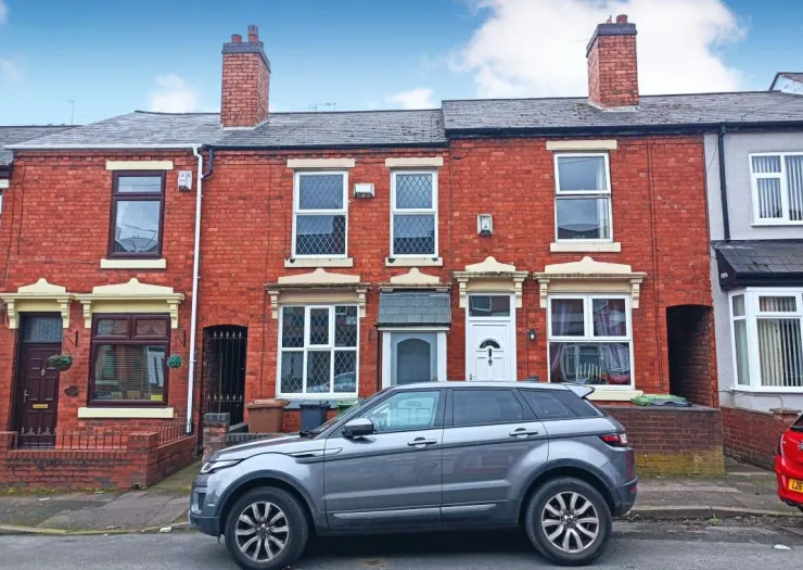Red brick terraced house exterior with white window frames and parked car.