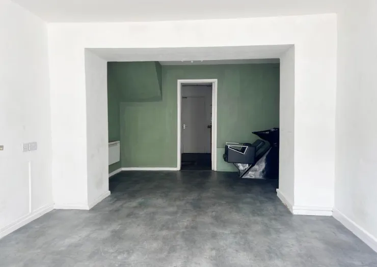 Empty commercial space with gray concrete floor, green walls, salon chair, and doorway to back room.