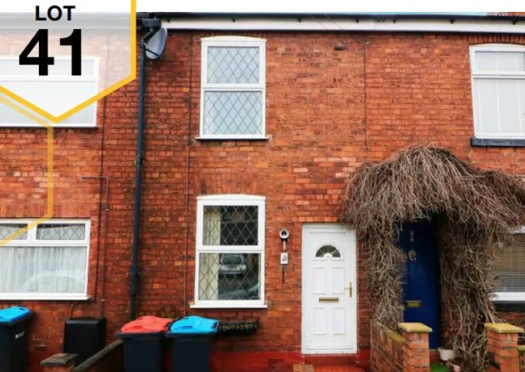 Red brick terraced house (Lot 41) with white front door and overgrown archway.