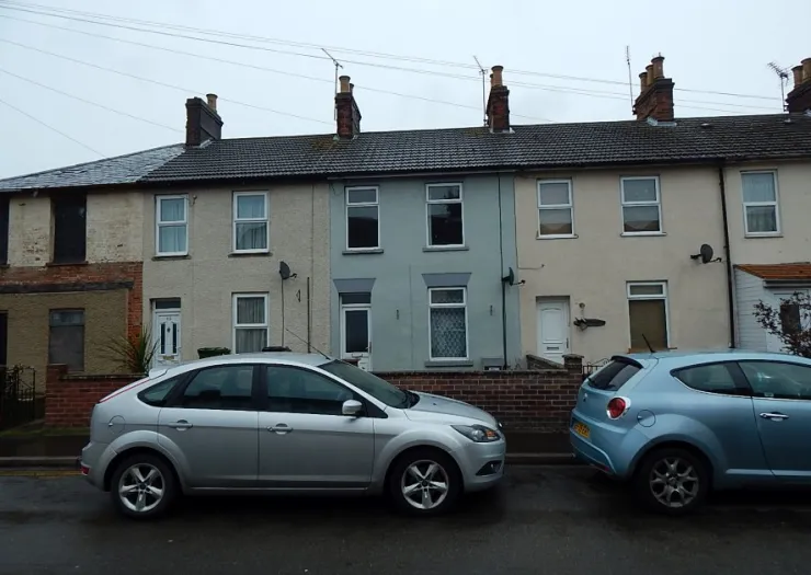 Row of terraced houses with a light blue/grey centre house. Cars parked on street.