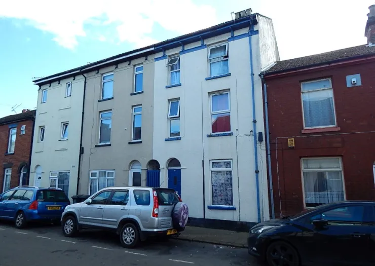 Row of terraced houses with beige and white exteriors, blue trim, and parked cars.