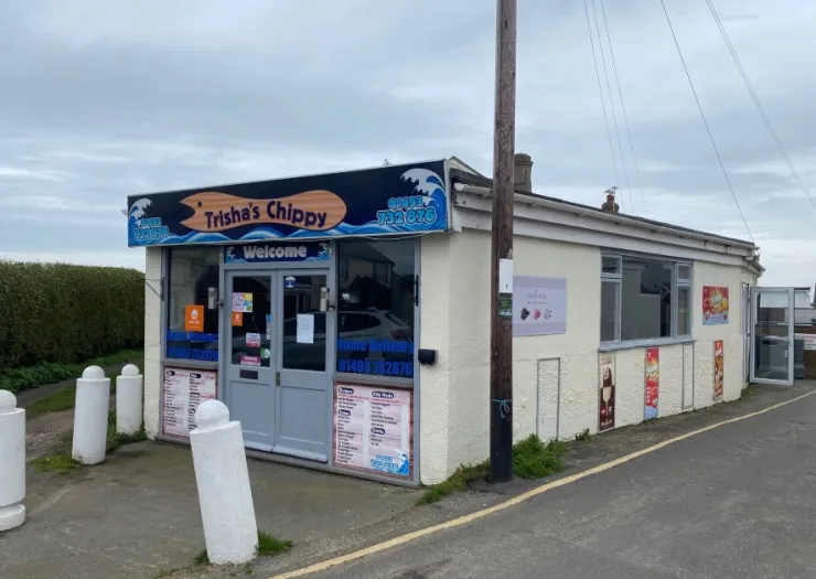 Trisha's Chippy storefront with "Welcome" sign, menu, and bollards.