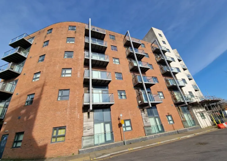 Modern red brick apartment building with balconies, under a clear blue sky.
