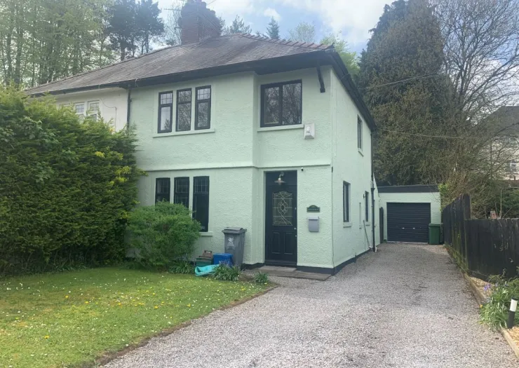 Light green semi-detached house with black trim, front garden, and attached garage.