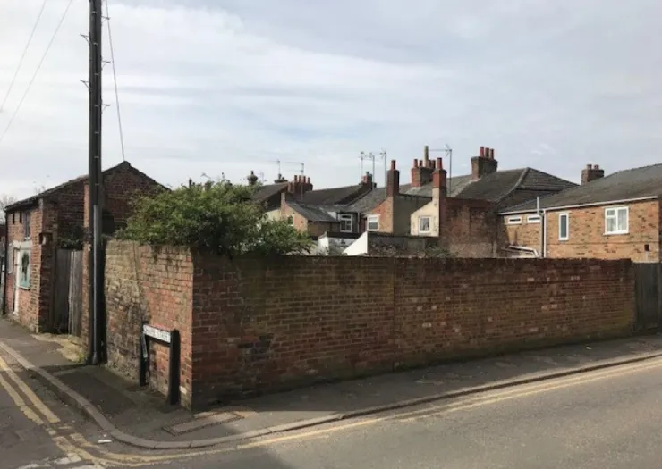 Brick wall and backs of terraced houses seen from a residential street corner.