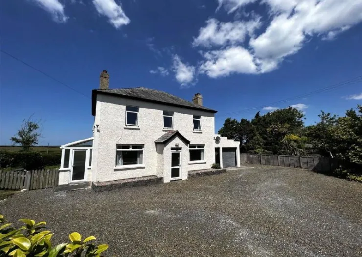White two-story house with gravel driveway, sunroom, and attached garage under blue sky.