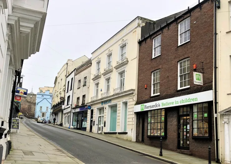 Barnardo's charity shop on a sloped high street with other businesses, including Barclays bank.