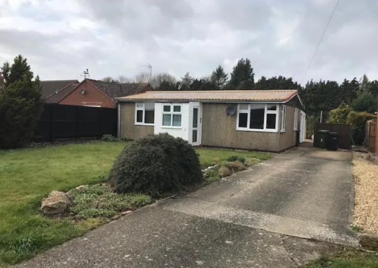 Single-story bungalow with a tan roof, white windows, front lawn, and paved driveway.
