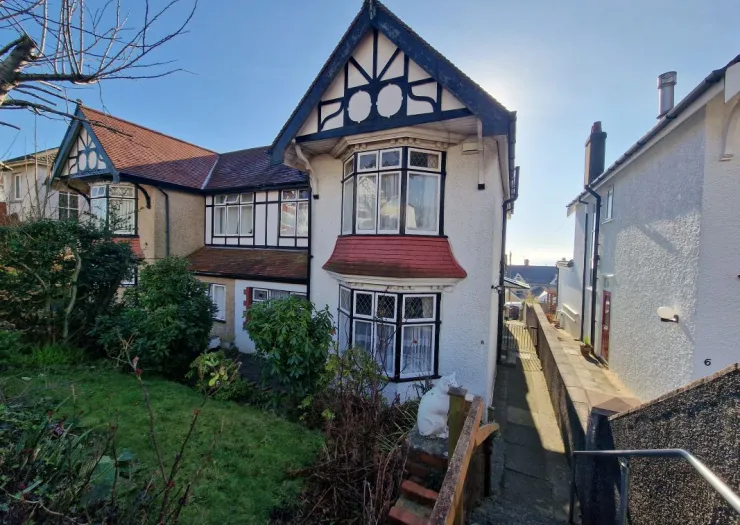 White detached house with mock Tudor features, bay windows, front garden, and a side path.