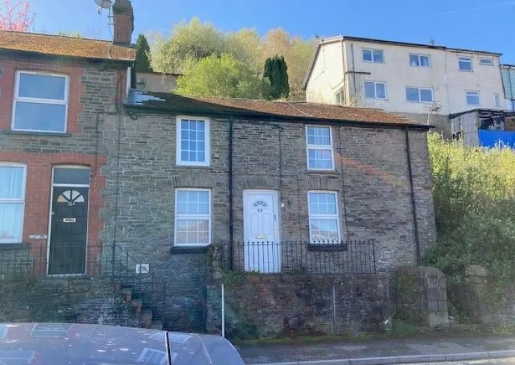Stone terraced cottage exterior with white door and windows, set against green hillside.
