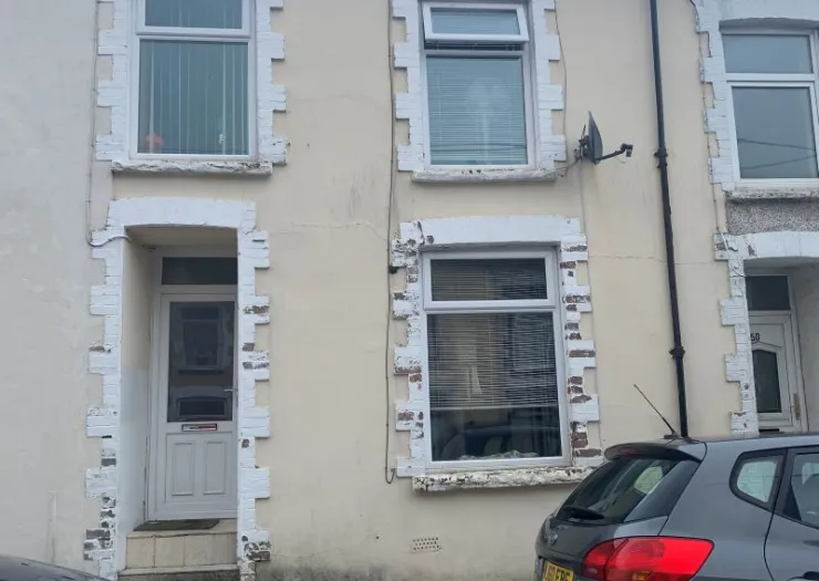 Beige terraced house exterior with white-framed windows and door.