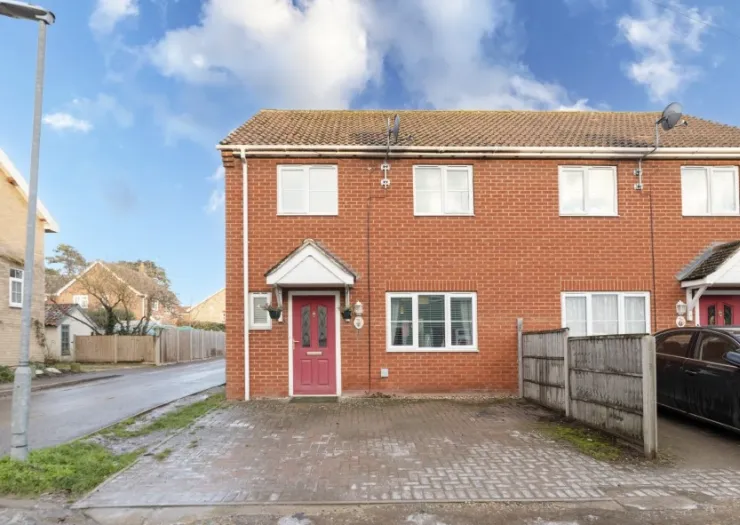 Red-brick terraced house with white porch and driveway.