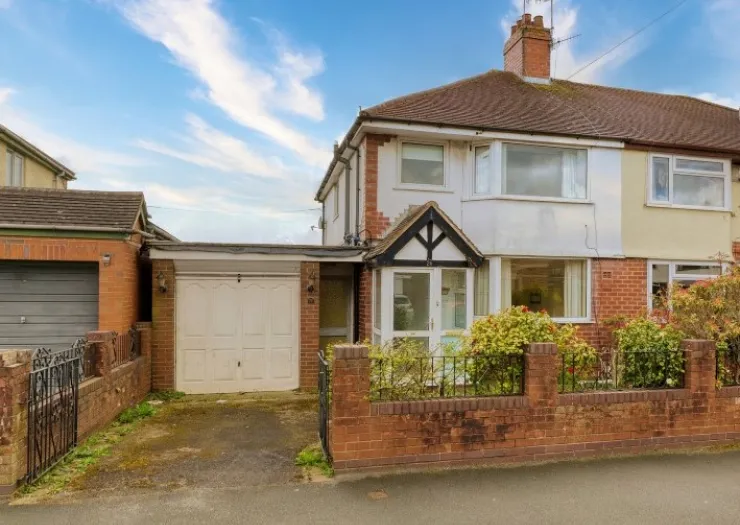 Suburban semi-detached house with attached garage, front garden, and brick wall.