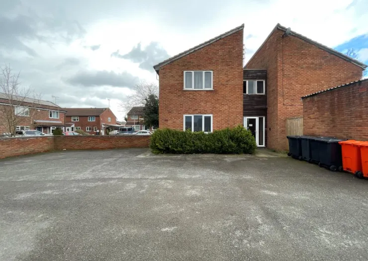 Red brick duplex with a large paved front area and some bins. Other terraced houses are visible in the background.