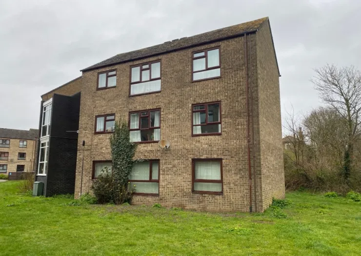 Exterior of a brown brick apartment building with dark brown window frames and a small grassy area.