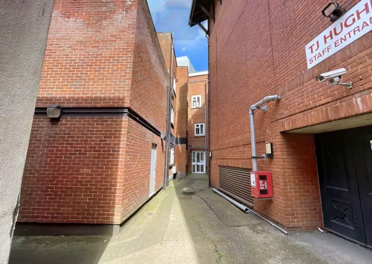 Narrow alleyway between red brick buildings, "TJ Hughes Staff Entrance" visible.
