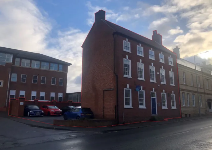 Red brick office building with parking lot, viewed from street corner.