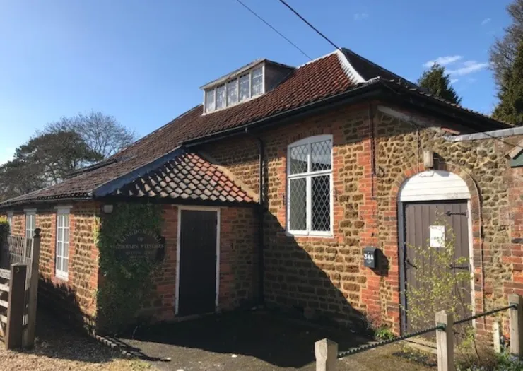 Brick and stone building with tiled roof, multiple windows, and "Kingdom Hall of Jehovah's Witnesses" sign.