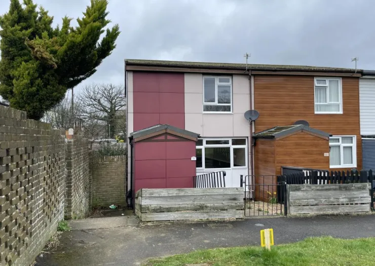Two-story terraced house with burgundy and wood-effect cladding, front garden, and small gate.