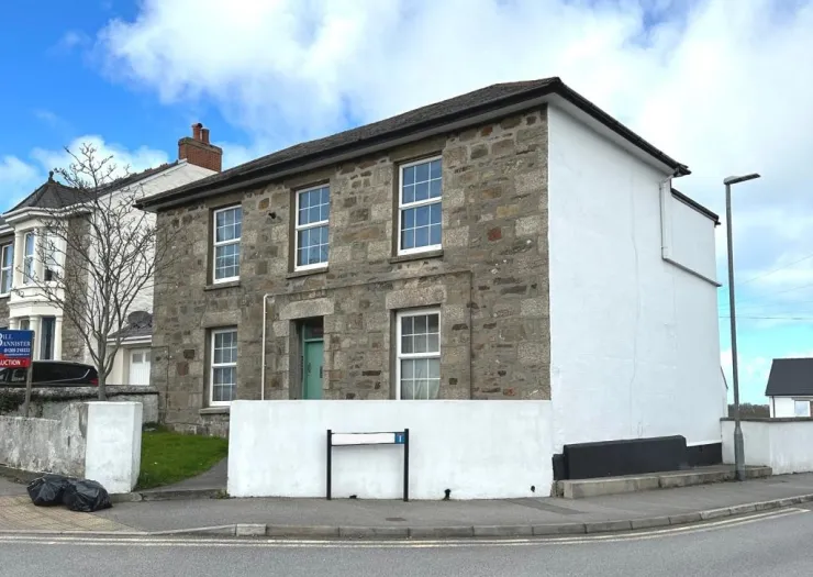 Stone house with white windows and partially painted white exterior wall, behind a low wall.