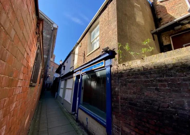 Narrow brick alleyway leading to a building with a blue storefront.