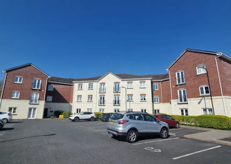 Modern apartment building exterior with balconies, parking lot, and cars on a clear sunny day.