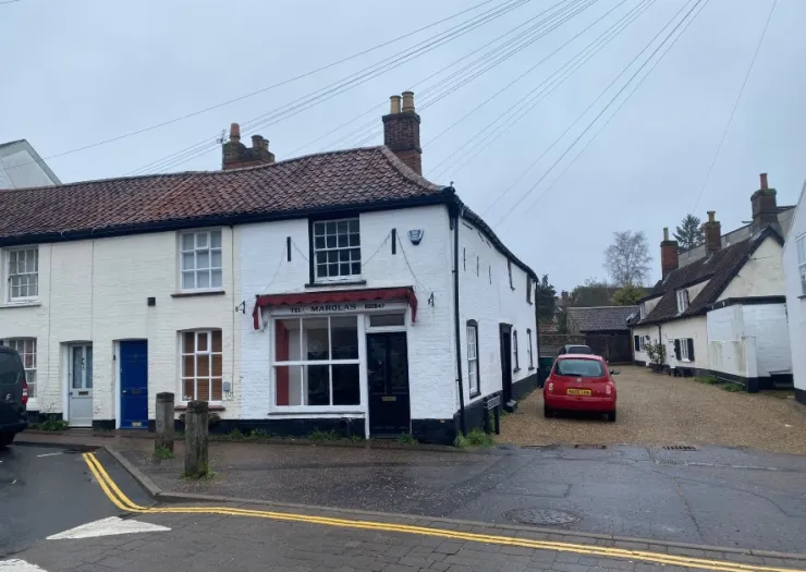 White detached building with "The Marolas" storefront and red tile roof. Red car parked in gravel driveway.