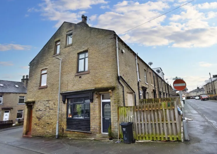 Stone terraced house exterior with black trim, wooden fence, and street view.