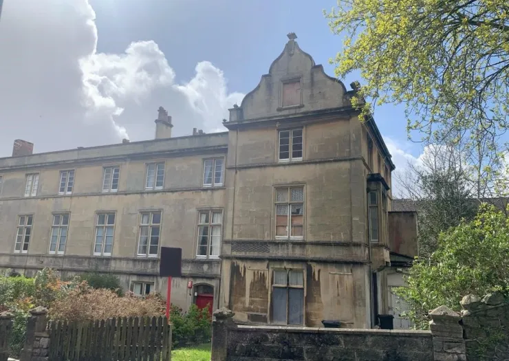 Grand stone building with unique Dutch gable, multiple windows, and a red door.