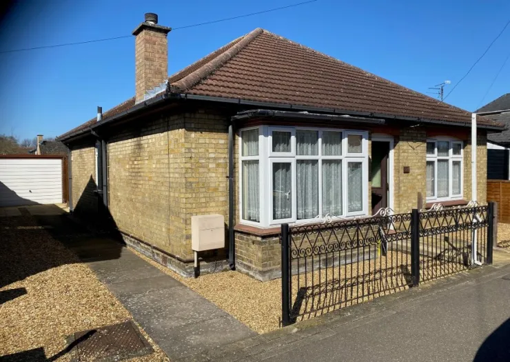 Yellow brick bungalow with bay window, decorative metal fence, and attached garage, on a sunny day.