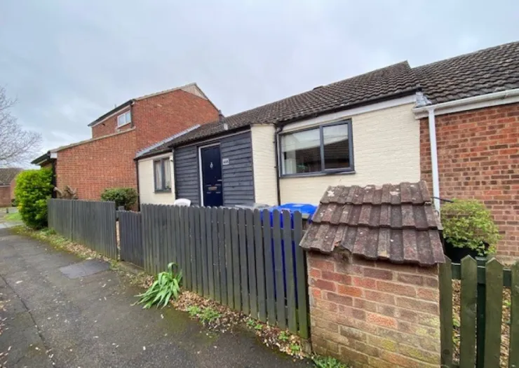 Exterior view of a single-story attached house with a dark gray fence and a blue door.