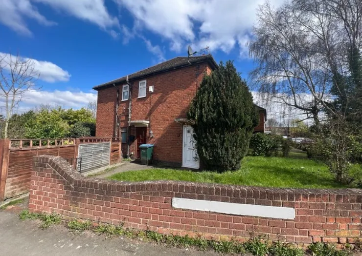 Red brick semi-detached house with front garden and brick wall under a blue sky.