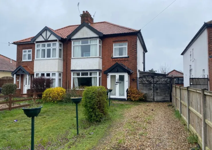 Red brick semi-detached house with white trim, front garden, and gravel driveway.