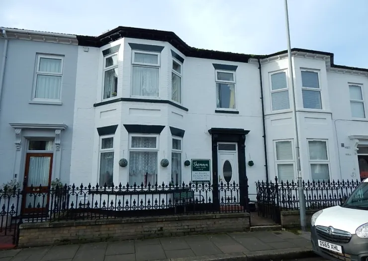 Shemara" guesthouse, white terraced house with bay window and black wrought iron fence.