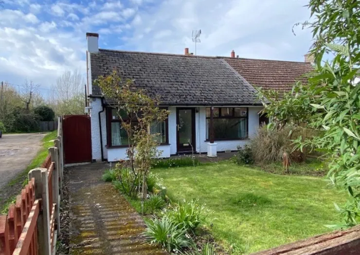 Single-story bungalow with tiled roof, white walls, and a front garden. Red gate and wooden fence.