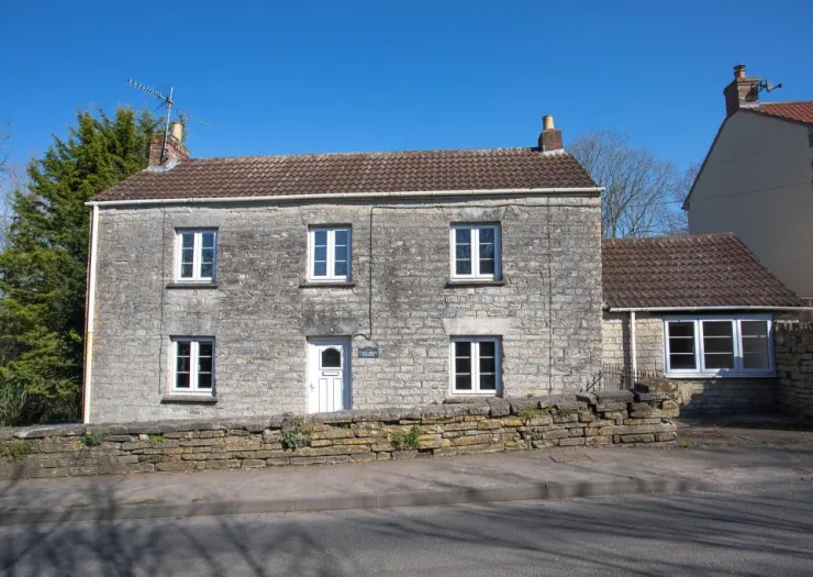 Stone cottage with white-framed windows and a tiled roof, behind a low stone wall.
