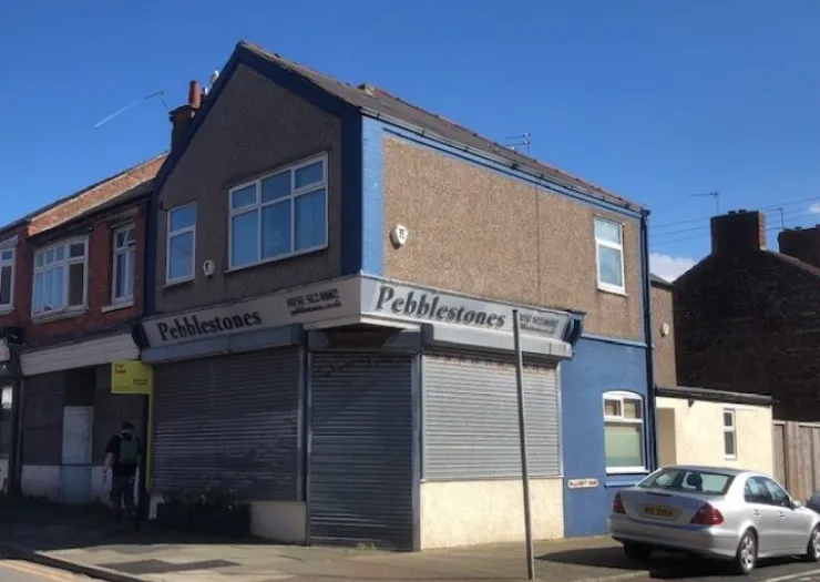 Pebblestones storefront with security shutters, corner location on a sunny day.
